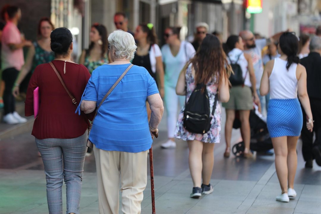 Una mujer mayor pasea del brazo de otra mujer por una calle de Madrid.